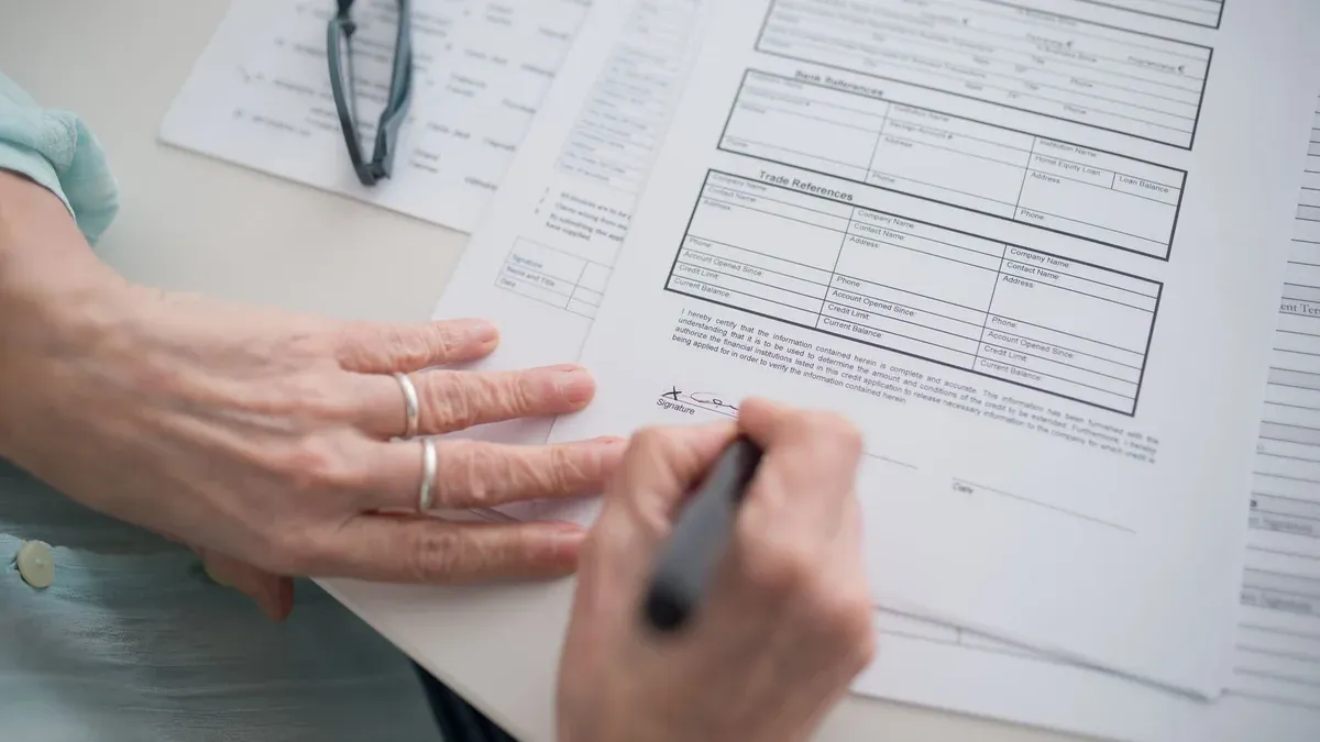 A close-up view of a hand signing official documents with a pen indoors.