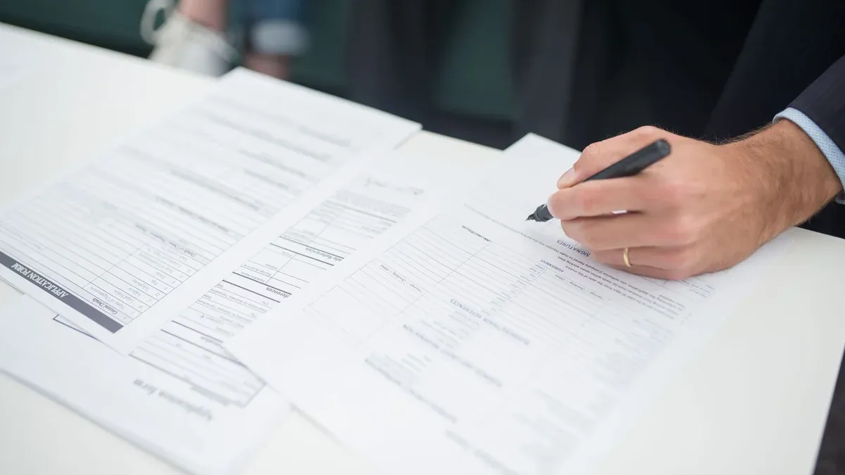 Close-up of a hand signing insurance documents in an office setting.