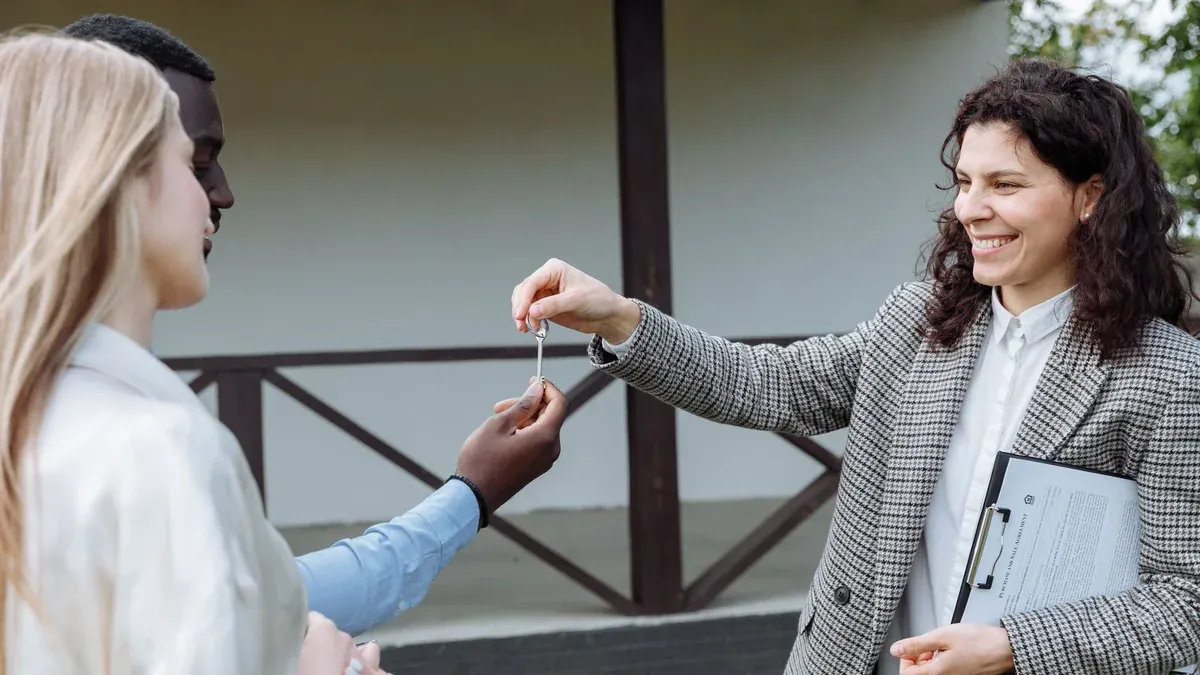 Real estate agent giving house keys to a happy couple outside their new home.