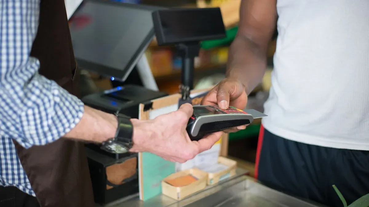 A customer making a payment with a credit card at a store checkout counter using a card reader.