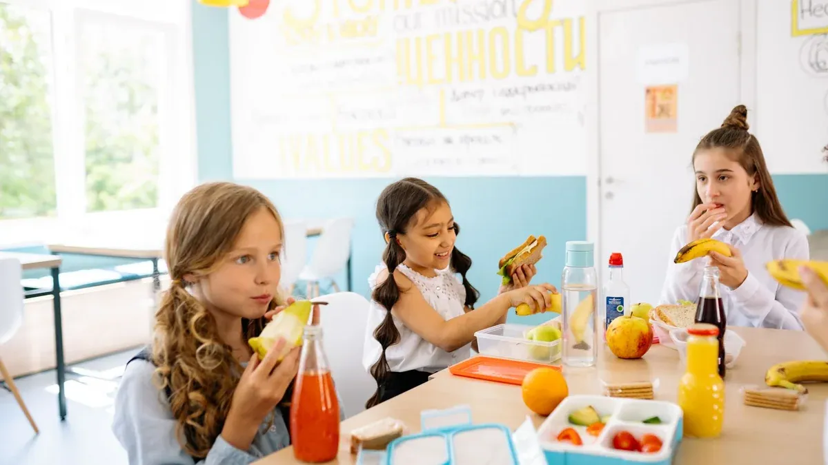 Group of schoolgirls having a break, eating healthy snacks at a canteen table.