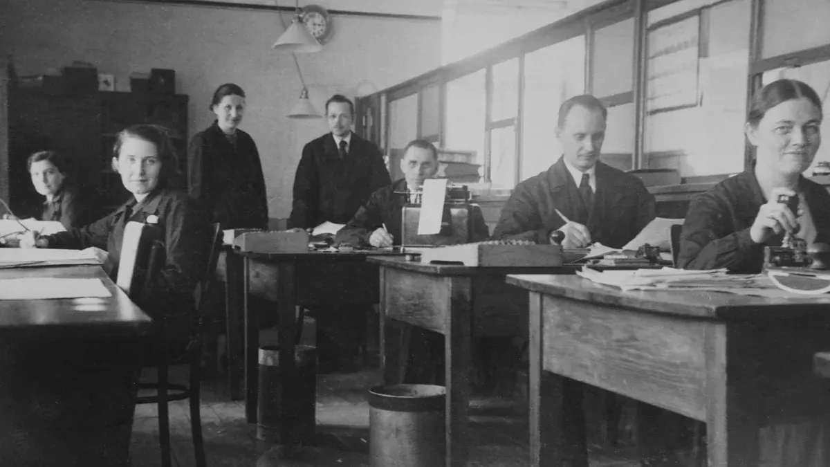 Retro black and white photo of office workers at desks, exuding a vintage workplace atmosphere.