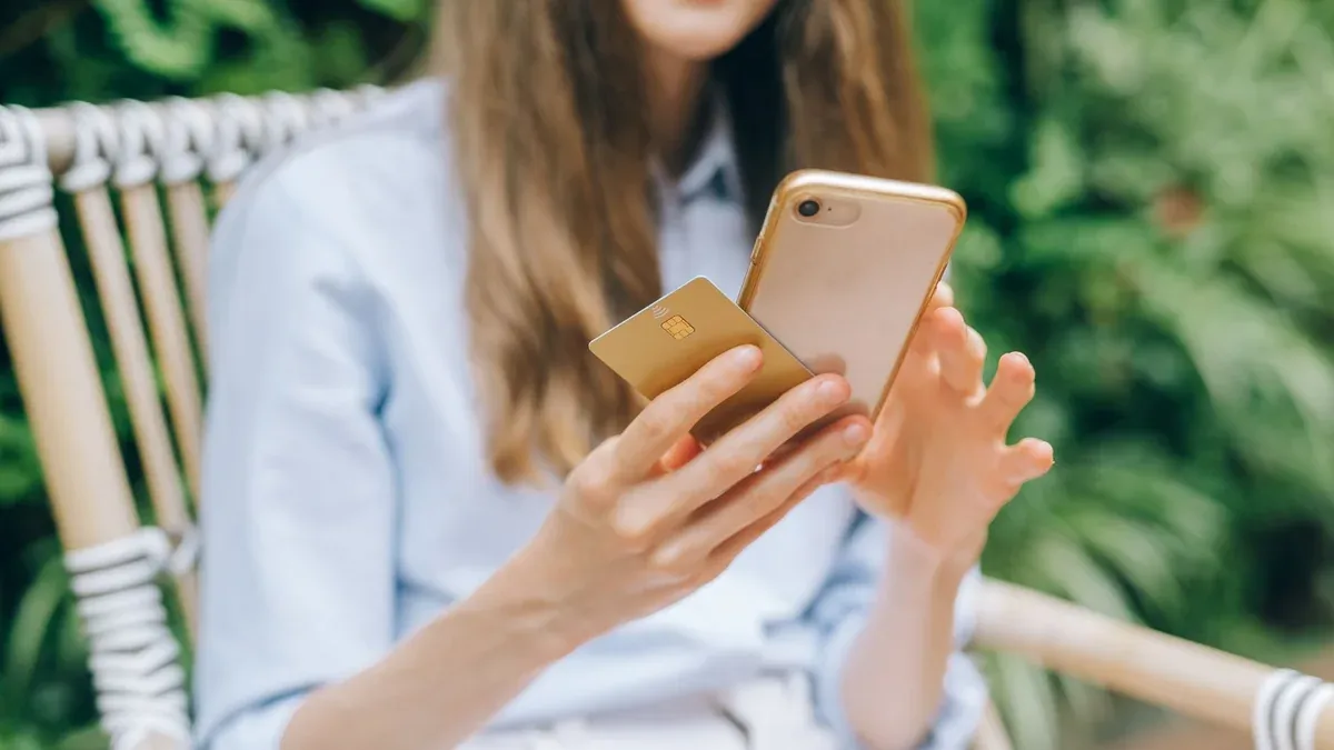 A woman making an online purchase using a smartphone and credit card outdoors.