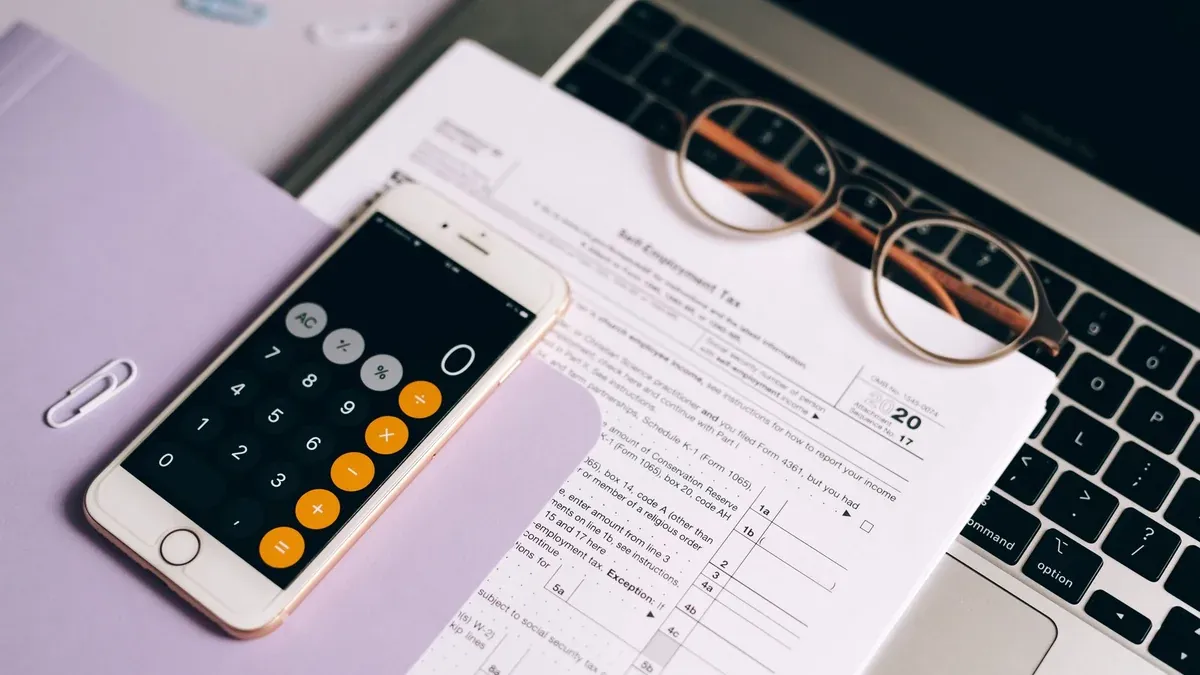 A smartphone with a calculator app on tax documents next to a laptop, emphasizing modern accounting.