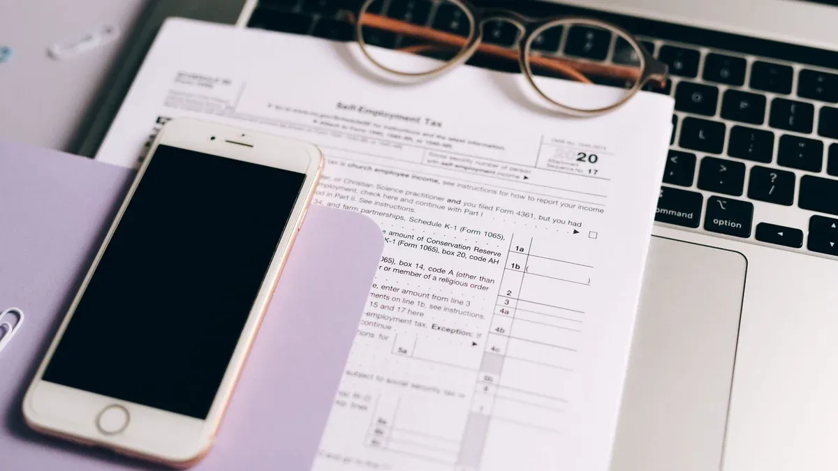 Close-up of tax documents with laptop and smartphone on a desk.