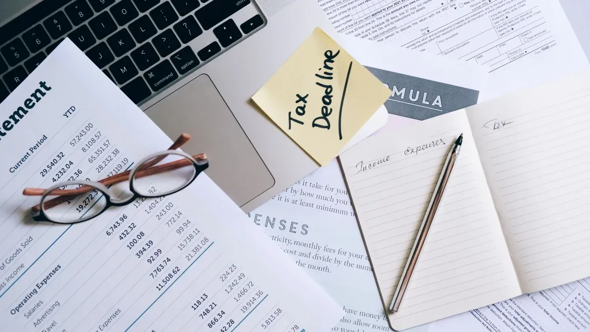 Workspace with laptop, documents, and tax deadline note for financial management.