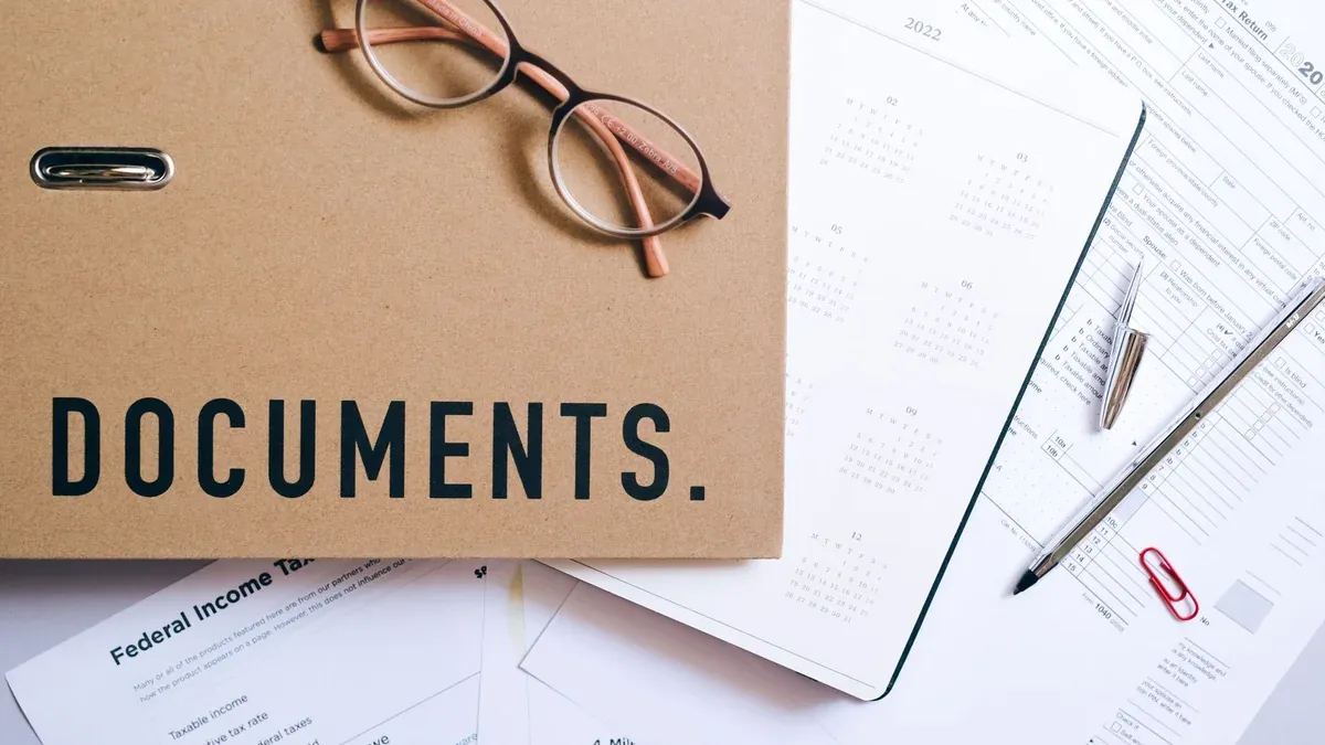 Flat lay of office supplies including documents, calendar, and eyeglasses on a desk.
