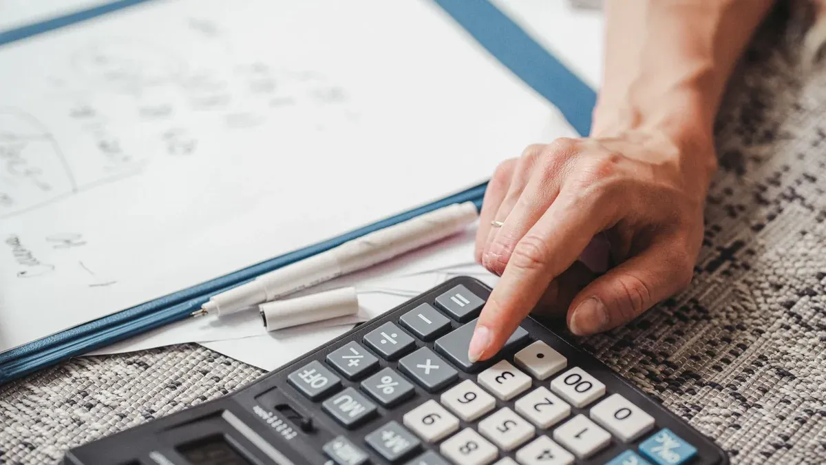A hand using a calculator on top of documents, indicating financial calculation or analysis.