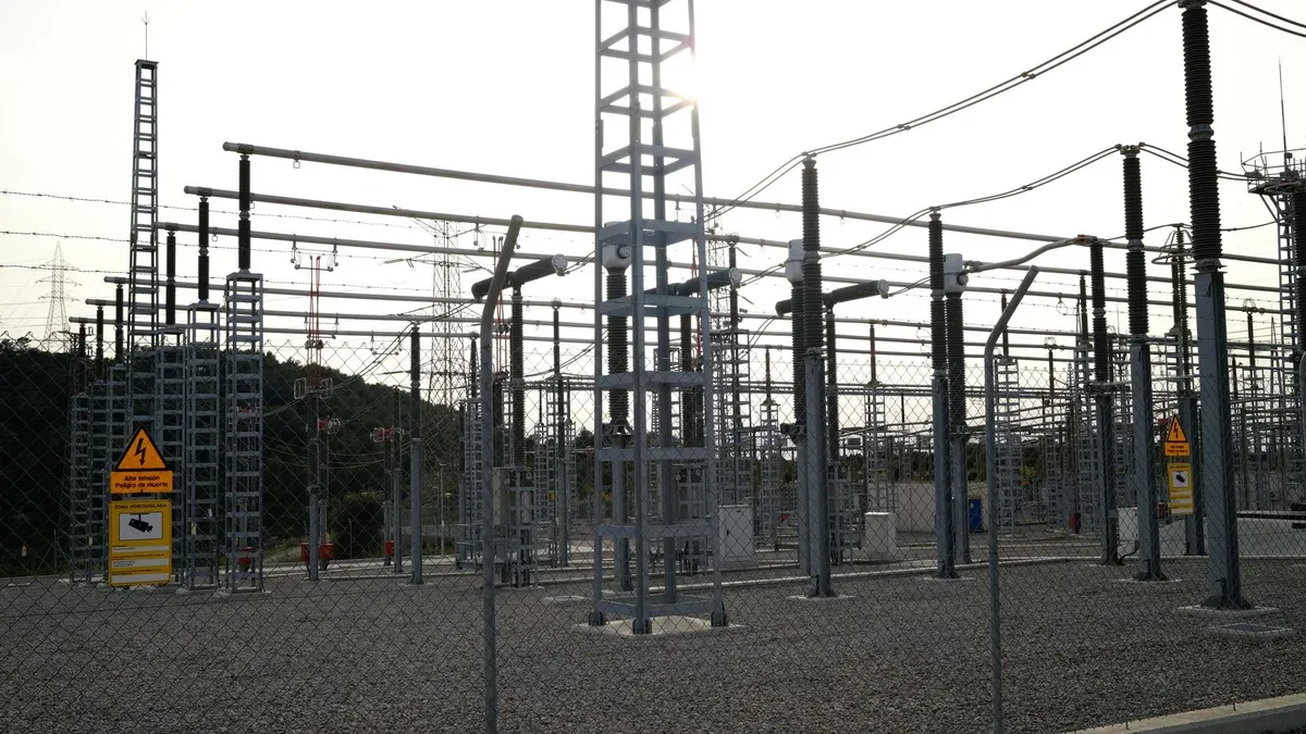 Outdoor electrical power substation with high voltage equipment and safety signs, surrounded by fencing.